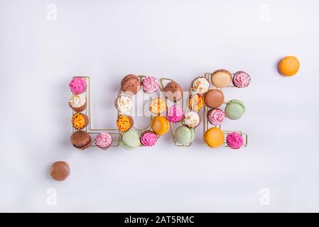 Top view composition of allsorts chocolate sweets with multicolored cream filling and cakes macaron arranged in wire shape of word Love on white backg Stock Photo