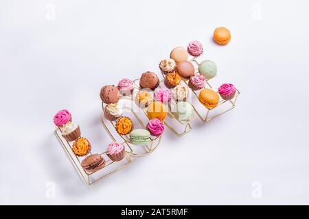 Top view composition of allsorts chocolate sweets with multicolored cream filling and cakes macaron arranged in wire shape of word Love on white backg Stock Photo
