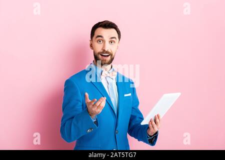cheerful bearded businessman holding digital tablet and gesturing on pink Stock Photo