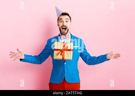 happy businessman in party cap throwing in air present on pink Stock Photo