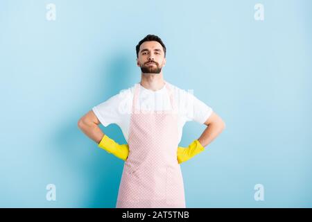 handsome bearded man in apron standing with hands on hips on blue Stock Photo