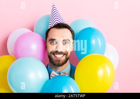cheerful bearded man in party cap near colorful balloons isolated on pink Stock Photo