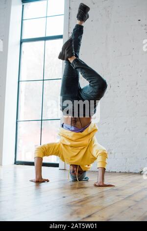 stylish man in hat doing handstand while breakdancing in dance studio Stock Photo