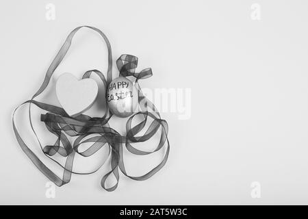 Black and White image. Easter egg with ribbon on a white background. Minimal easter concept. Flat lay, top view. Stock Photo