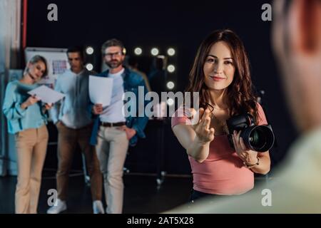 selective focus of happy photographer gesturing while looking at model in photo studio Stock Photo