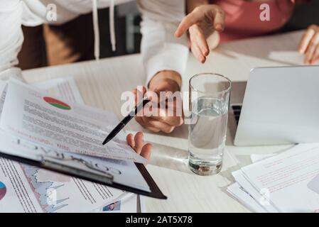 cropped view of art director pointing with finger at clipboard near assistant Stock Photo