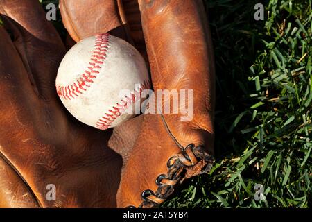 Antique leather baseball mitt with old baseball closeup on grass field Stock Photo