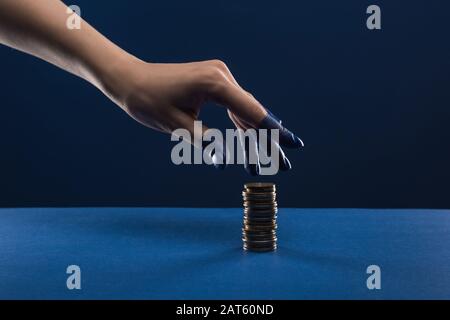 cropped view of female hand with painted fingers touching coins isolated on blue Stock Photo