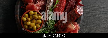 top view of delicious meat platter served with olives and herbs on wooden black table, panoramic shot Stock Photo