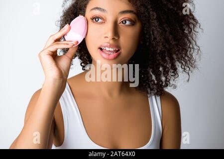 young african american woman using silicone cleansing facial brush, isolated on grey Stock Photo