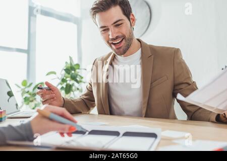 Selective focus of smiling ux designer developing mobile app prototype with colleague in office Stock Photo