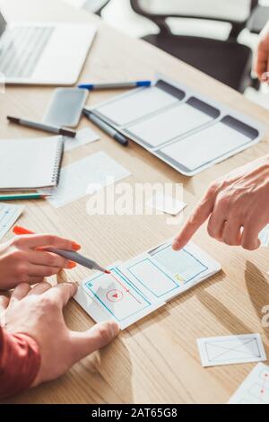Cropped view of ux designers developing mobile app with layouts on table Stock Photo