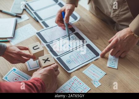 Cropped view of designers with mobile website wireframe sketches and cubes with ux letters on table Stock Photo