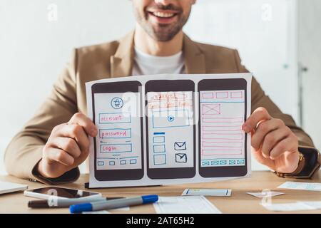 Cropped view of smiling designer showing mobile website wireframe sketches at table Stock Photo