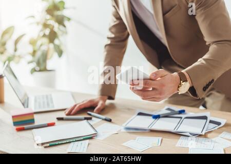Cropped view of ux designer using smartphone by website wireframe sketches on table Stock Photo