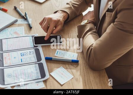 Cropped view of designer using smartphone while developing user experience design at table Stock Photo