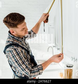 handsome installer measuring white kitchen cabinet Stock Photo