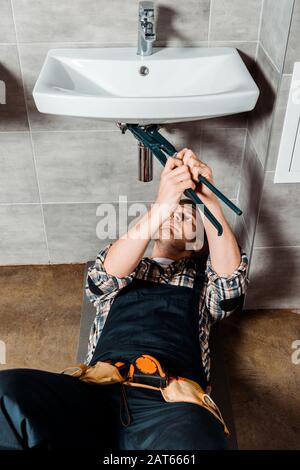 focused installer holding slip joint pliers near pipe in bathroom Stock Photo