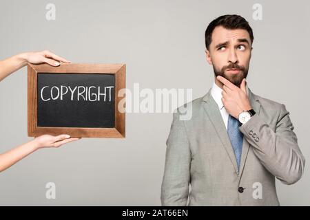 partial view of woman holding chalkboard with copyright inscription near thoughtful businessman isolated on grey Stock Photo