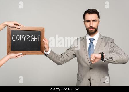 cropped view of woman holding chalkboard with copyright inscription near businessman looking at camera isolated on grey Stock Photo