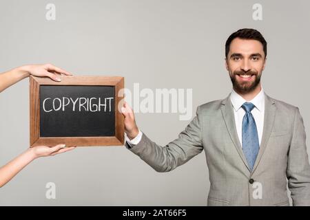 cropped view of woman holding chalkboard with copyright inscription near businessman smiling at camera isolated on grey Stock Photo