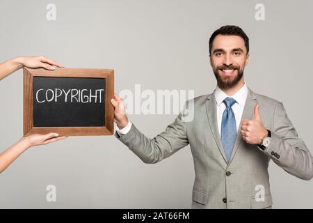 cropped view of woman holding chalkboard with copyright inscription near businessman showing thumb up isolated on grey Stock Photo