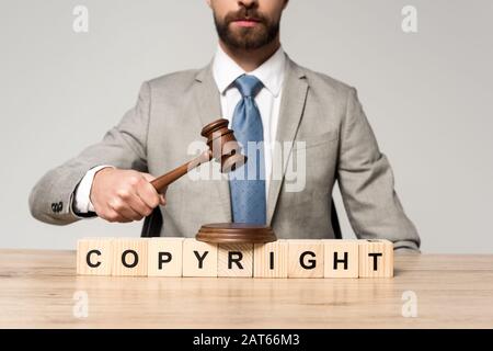 cropped view of judge holding gavel near wooden cubes with copyright inscription isolated on grey