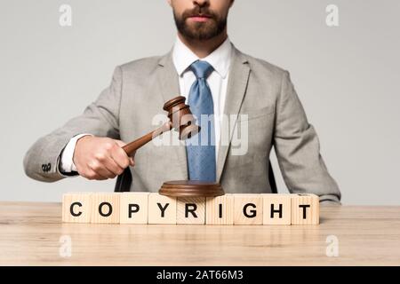 cropped view of judge holding gavel near wooden cubes with copyright inscription isolated on grey Stock Photo