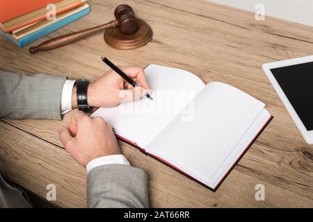 cropped view of lawyer writing in notebook on wooden desk Stock Photo