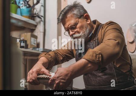 selective focus of senior cobbler fixing sole to shoe in workshop Stock Photo