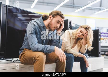 sad boyfriend and girlfriend sitting near new tv in home appliance store Stock Photo