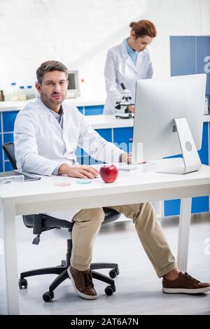 selective focus of molecular nutritionist looking at camera and his colleague on background Stock Photo