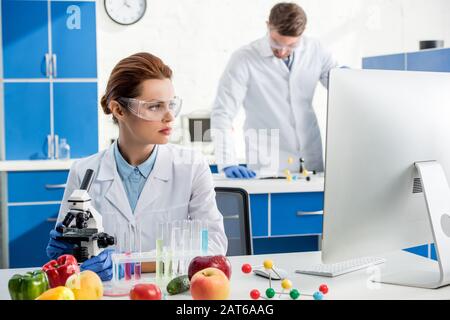 selective focus of molecular nutritionist looking at computer and colleague on background Stock Photo