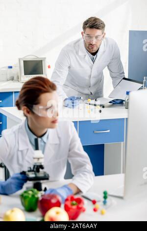 selective focus of molecular nutritionist looking at colleague in lab Stock Photo