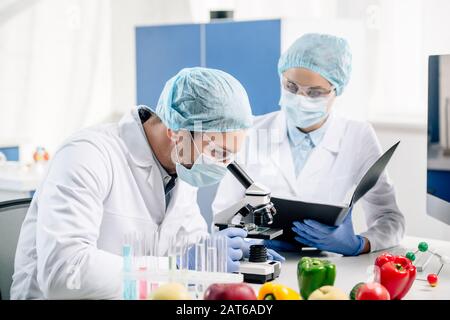 molecular nutritionist holding folder and looking at colleague with microscope Stock Photo