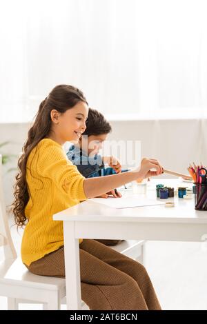 adorable brother and sister sitting at table and drawing together Stock Photo
