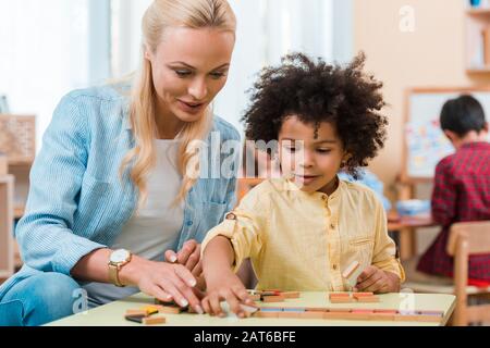 Selective focus of teacher helping to african american kid with wooden game in montessori class Stock Photo