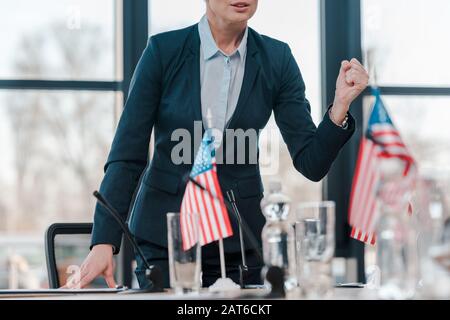 cropped view of diplomat with clenched fist talking while standing near microphone and american flags Stock Photo