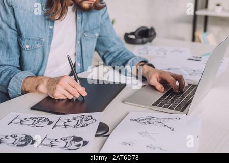 cropped view of animator using gadgets near sketches Stock Photo