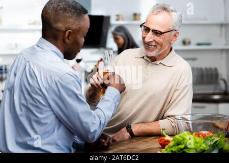 african american man clinking with his smiling friend in kitchen Stock Photo