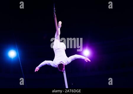 acrobat performing upside down on metallic pole in arena of circus Stock Photo