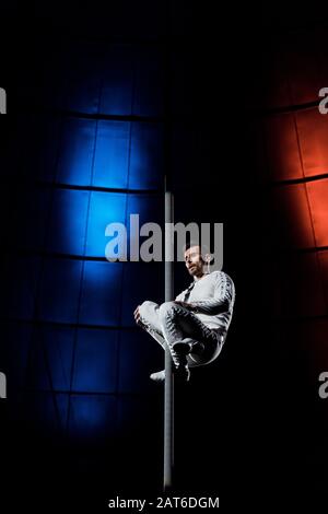 handsome and strong acrobat performing on metallic pole Stock Photo