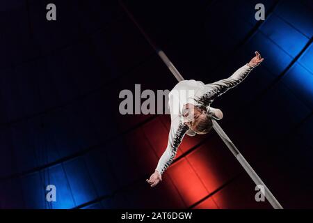 low angle view of strong acrobat with outstretched hands performing on metallic pole Stock Photo
