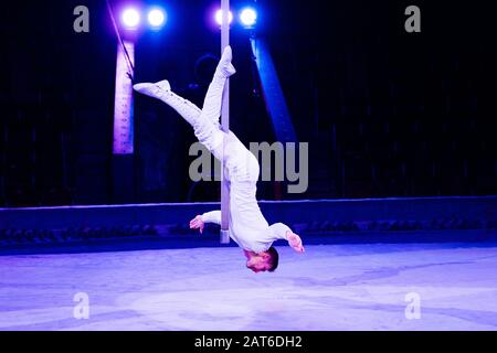 acrobat performing upside down on pole in arena of circus Stock Photo