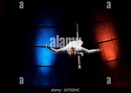 strong acrobat with outstretched hands performing on metallic pole Stock Photo
