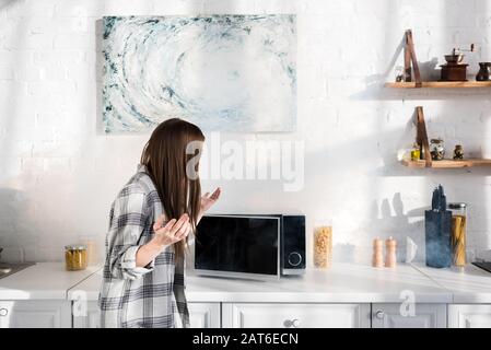 shocked woman looking at broken microwave in kitchen Stock Photo