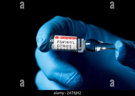 Fentanyl citrate injection ampule held by gloved hand of healthcare worker with dark background. Stock Photo