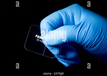 Gloved hand of nurse holds fentanyl transdermal patch on dark background. Stock Photo