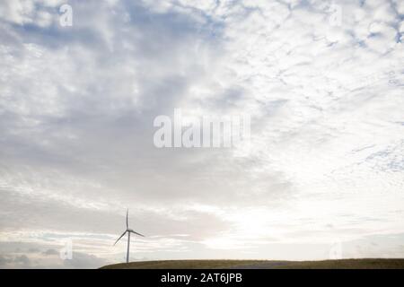 a wind turbine used in energy production on a hill with setting sun behind Stock Photo