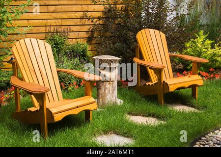 Pair of wooden Adirondack chairs on green grass lawn with grey flagstone footpath in backyard garden summer Stock Photo